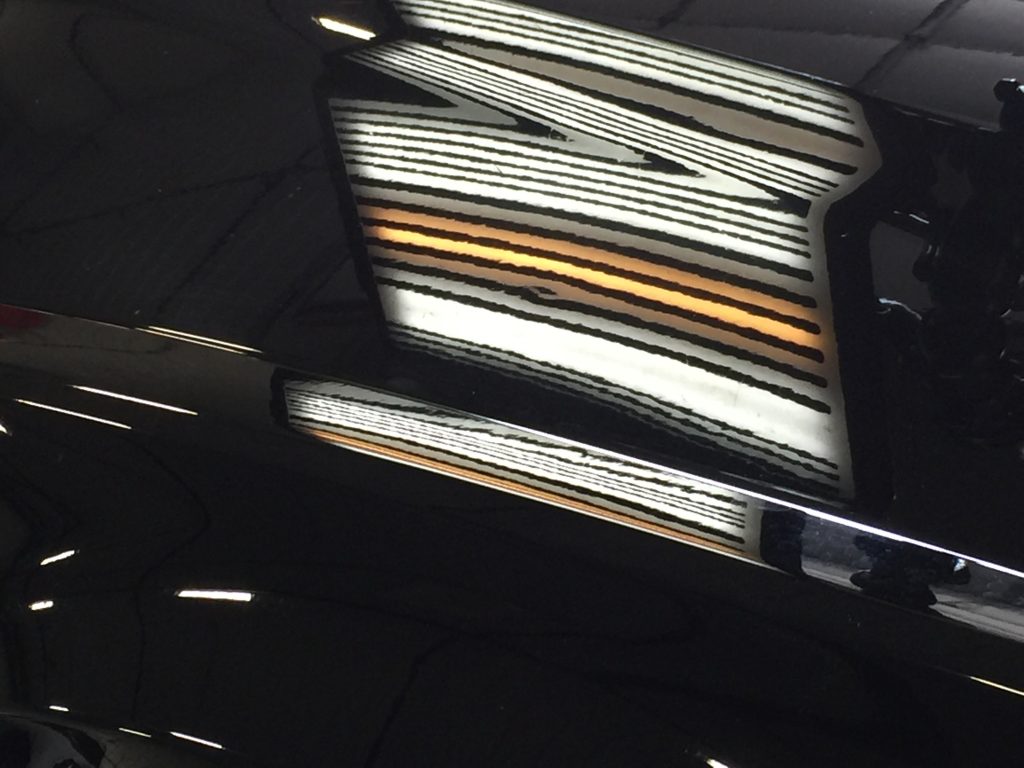 Hail dent on the aluminum hood of a 2016 Chrysler 300 C under a PDR light board