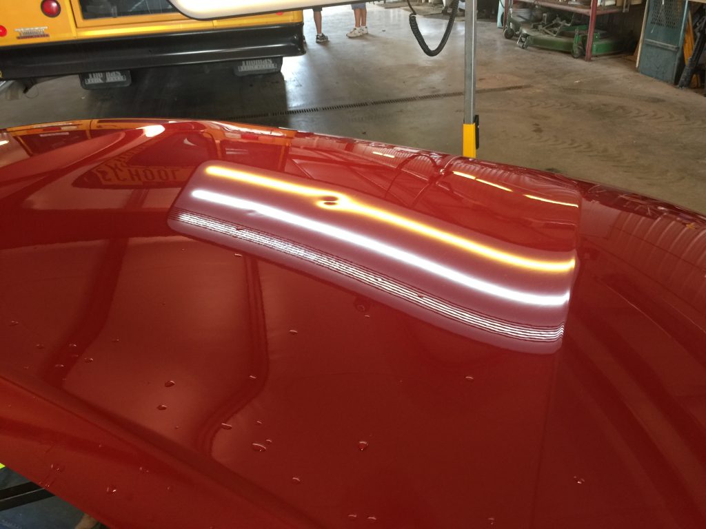 Dents on the red hood of a 2010 Toyota Tundra under a PDR light, possibly from falling walnuts or acorns