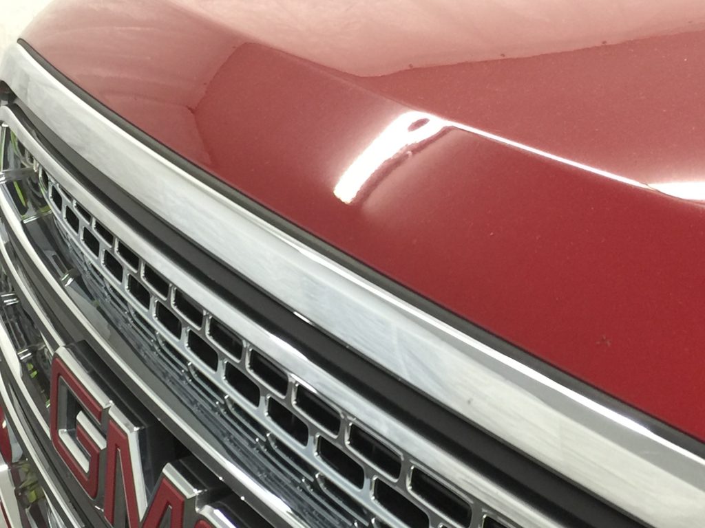 Dent in the aluminum hood of a red 2016 GMC Yukon, above the grille, before paintless repair