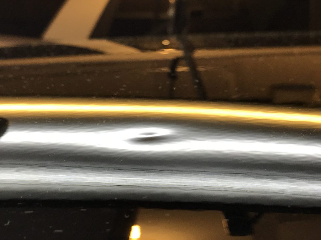 Small sharp dent in the roof of a 2016 Cadillac ATS under a PDR inspection light, caused by a falling acorn
