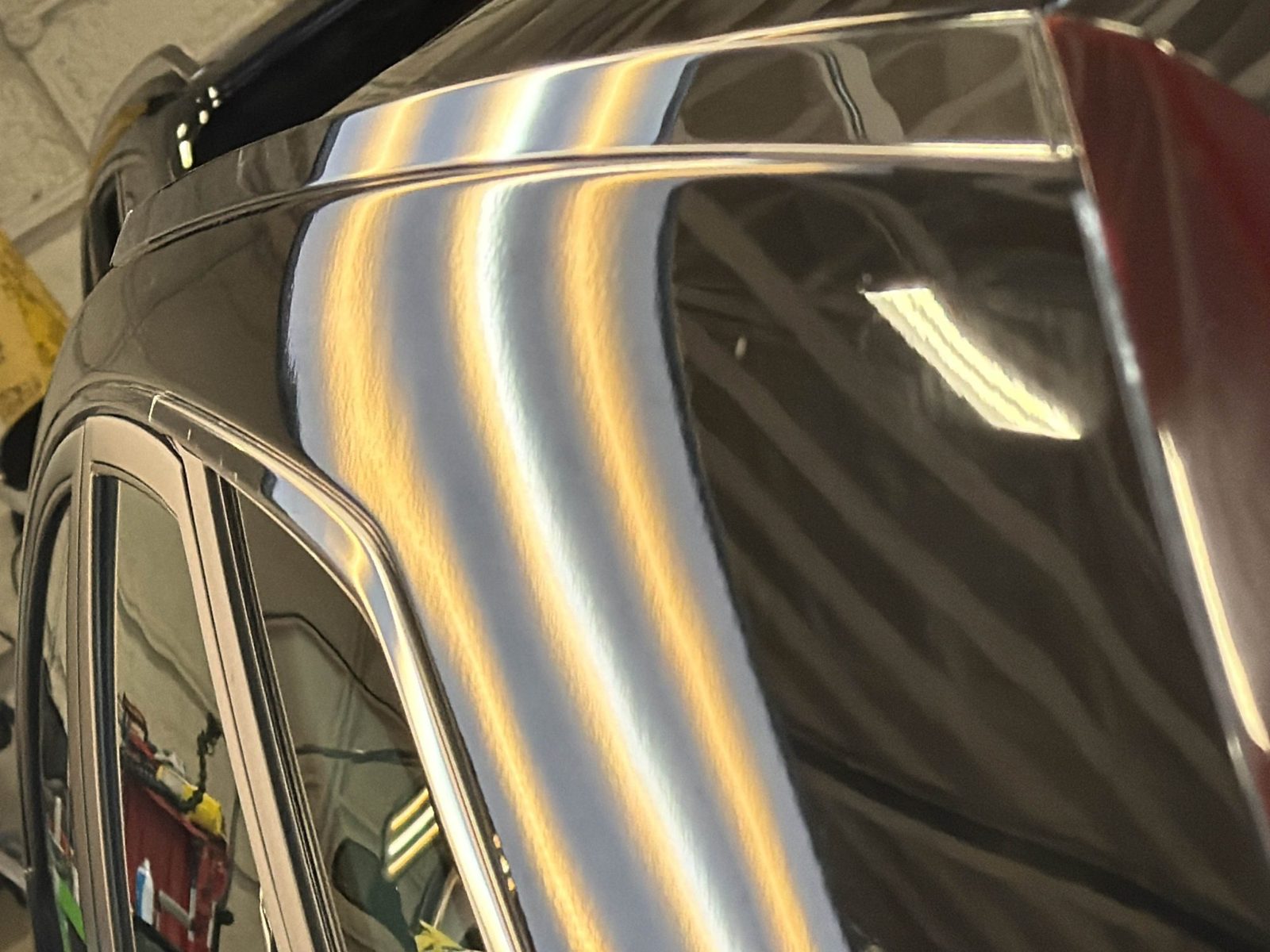 Driver-side roof rail of a black Cadillac CTS Sport Wagon, hail dents visible in the reflection