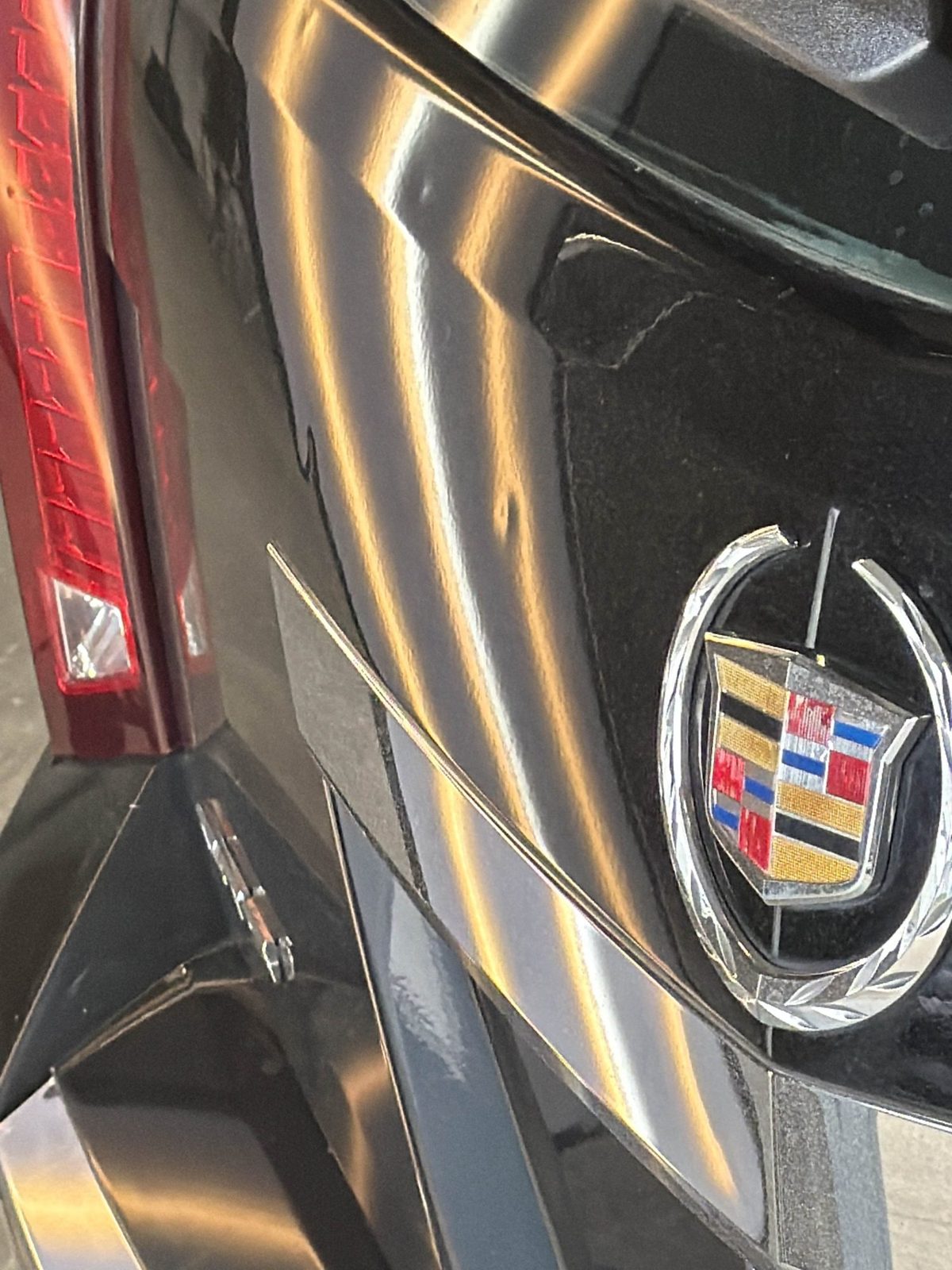 Steel lower liftgate of a black Cadillac CTS Sport Wagon by the Cadillac emblem, hail dents in the reflection