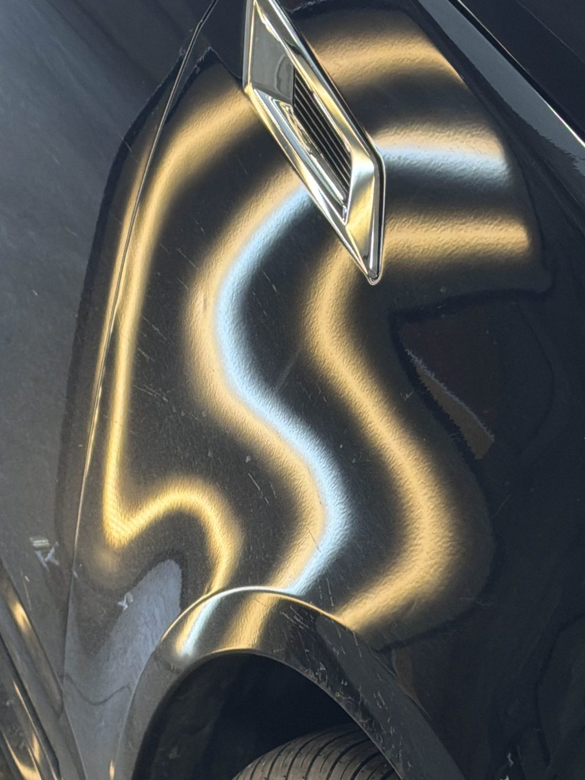 Steel passenger fender of a black Cadillac CTS Sport Wagon with a heavily distorted reflection from hail dents