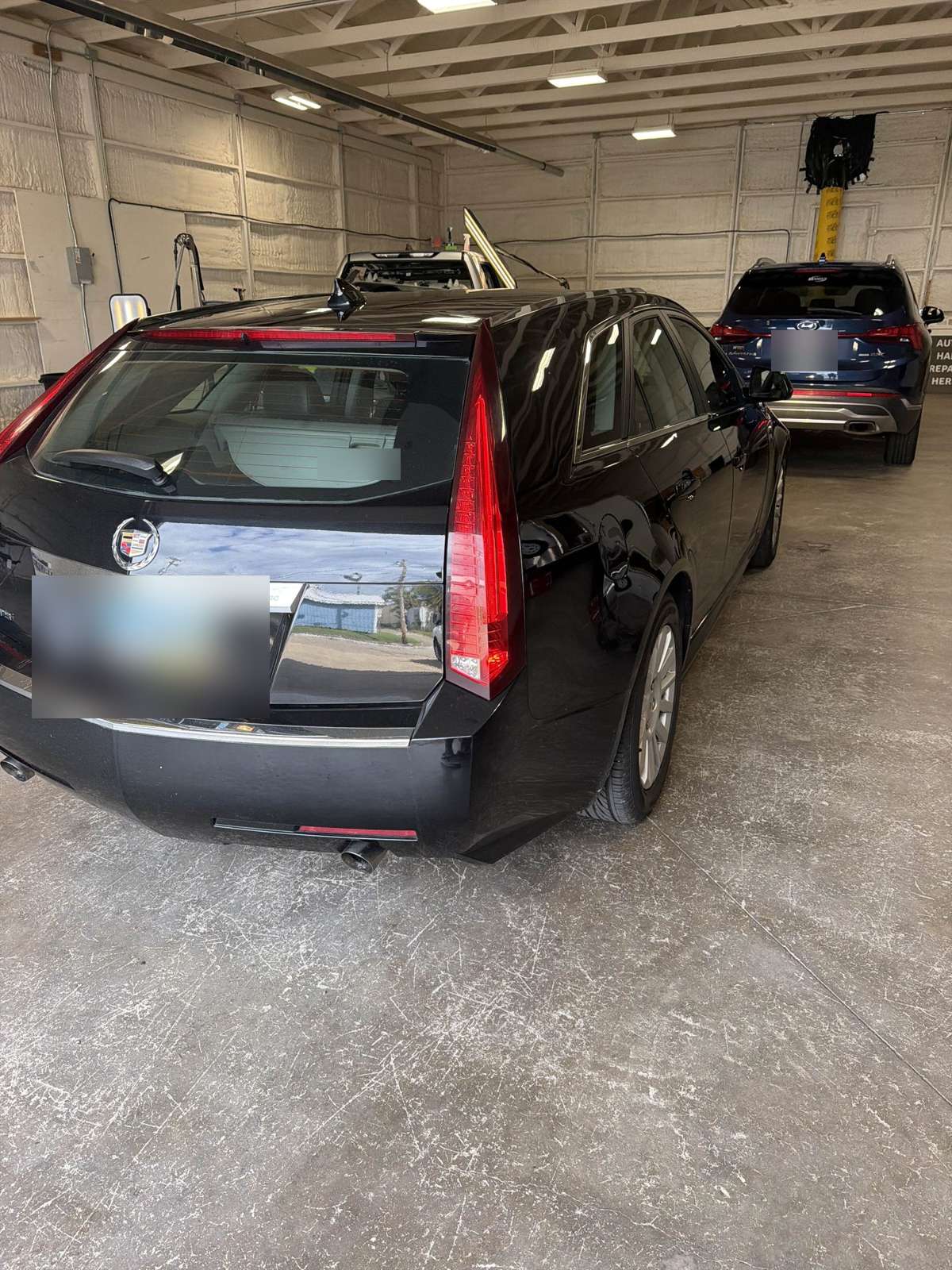 Black 2012 Cadillac CTS Sport Wagon in the 217 Dent shop, passenger-side rear corner view, license plates blurred