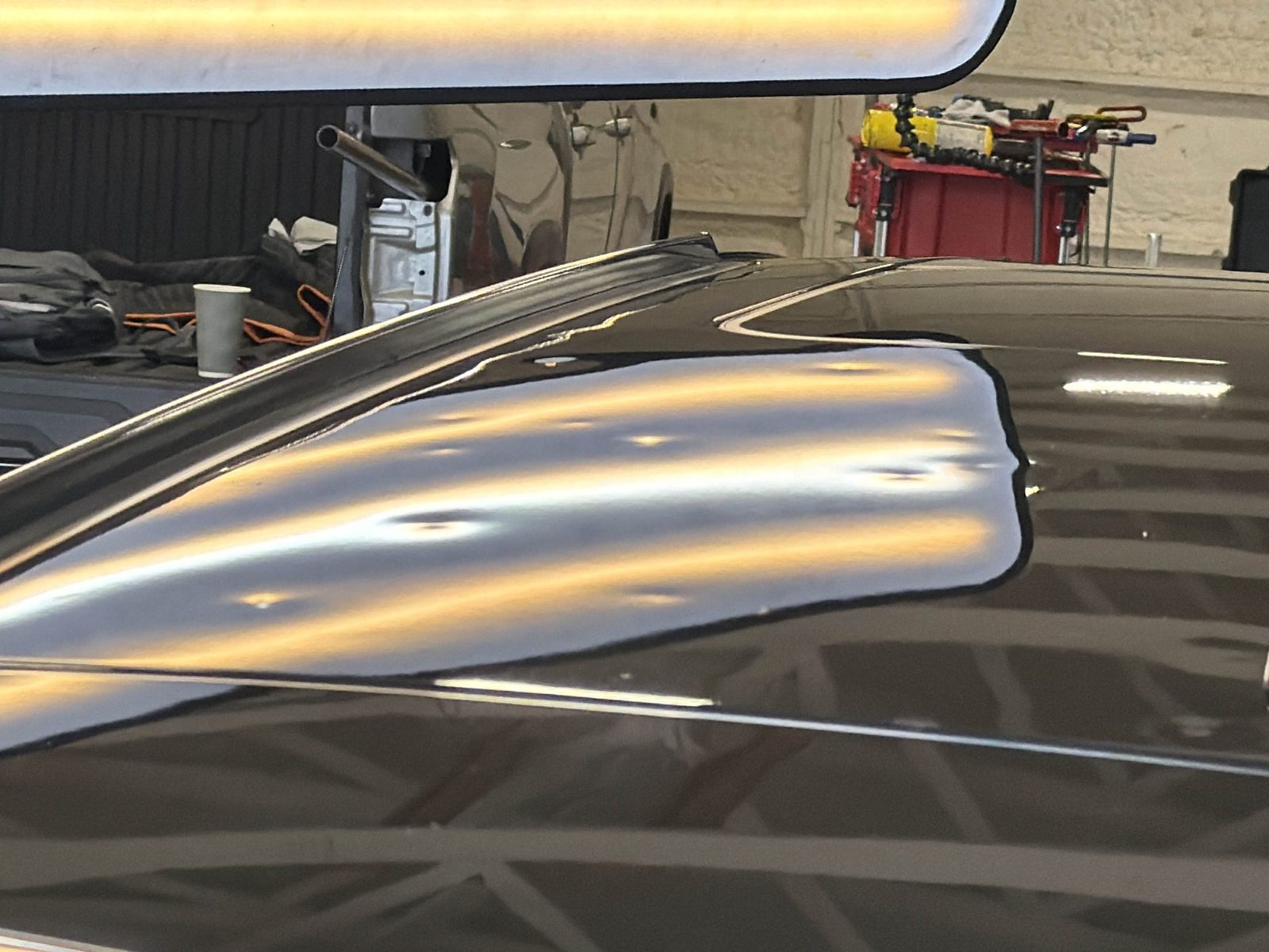 Steel roof of a black Cadillac CTS Sport Wagon under a PDR light board, with hail dents bending the reflected light lines