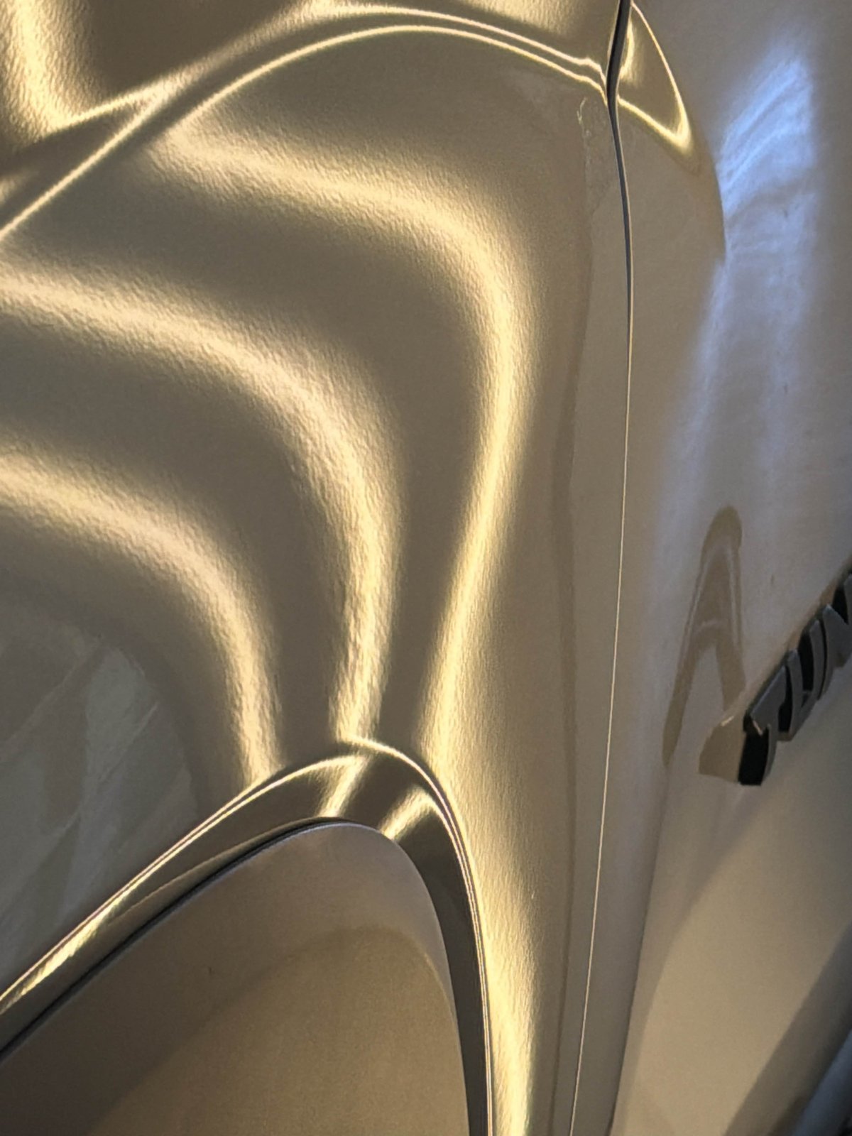 Driver fender of a silver 2024 Toyota Tundra with hail dents distorting the PDR light lines