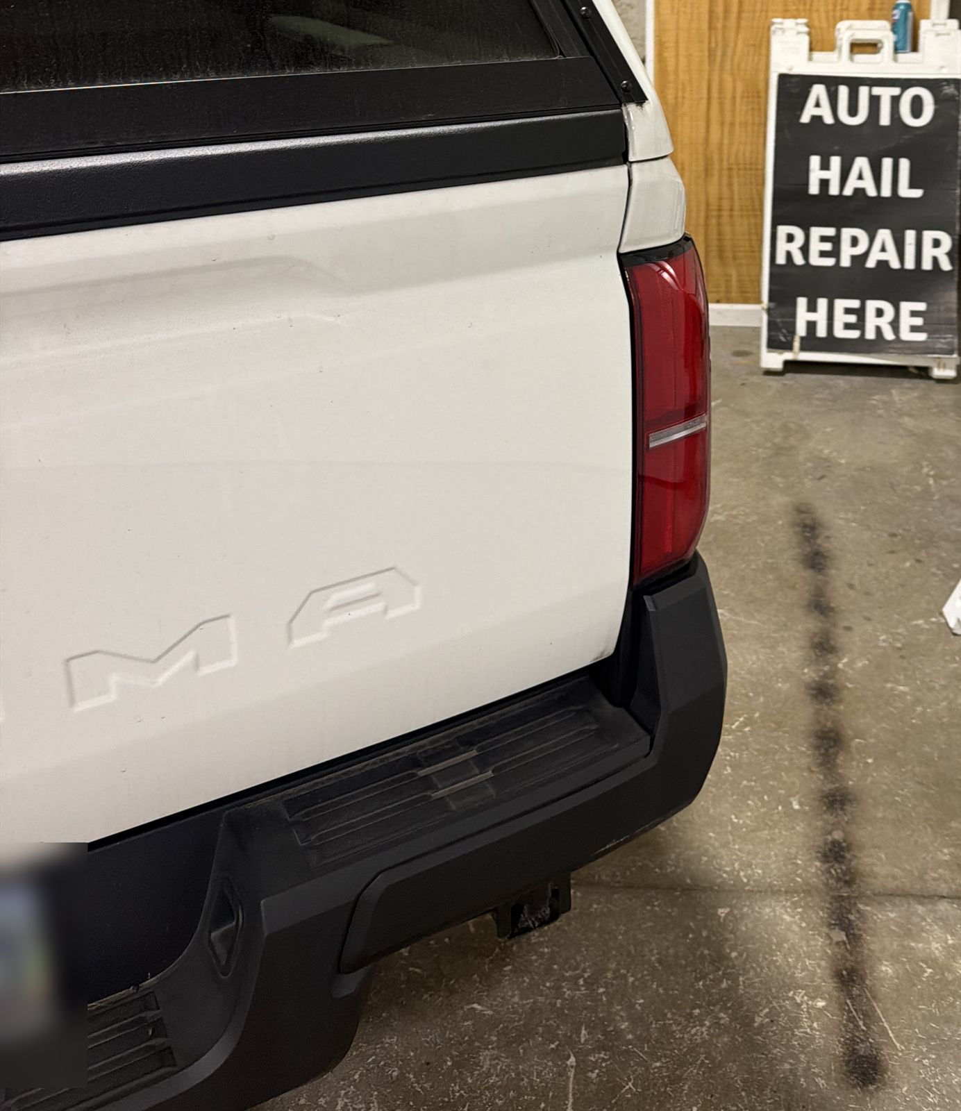 Tailgate of a white 2025 Toyota Tacoma SR next to an Auto Hail Repair Here sign in the 217 Dent shop