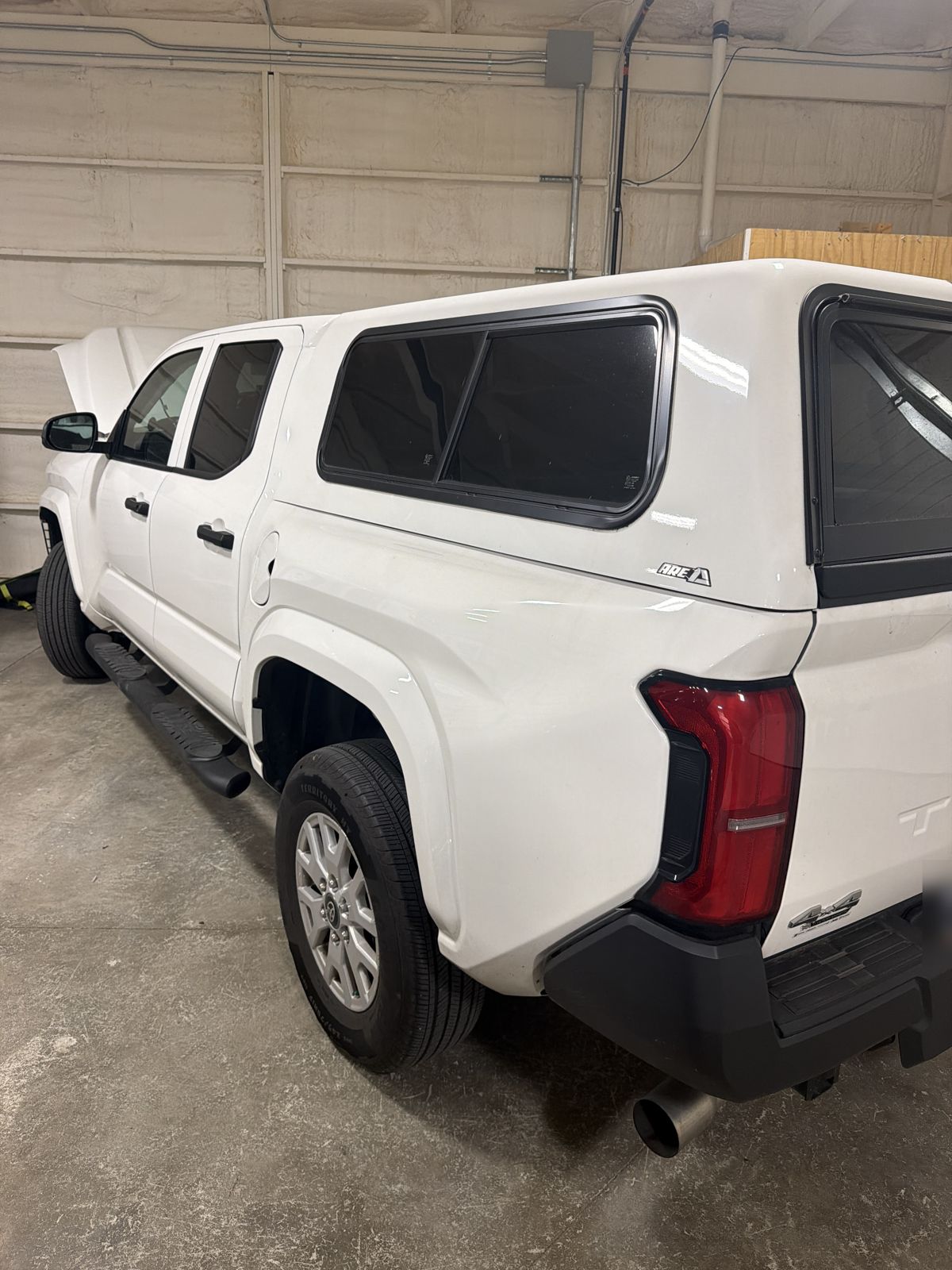 White 2025 Toyota Tacoma SR with a topper in the 217 Dent shop, rear corner view