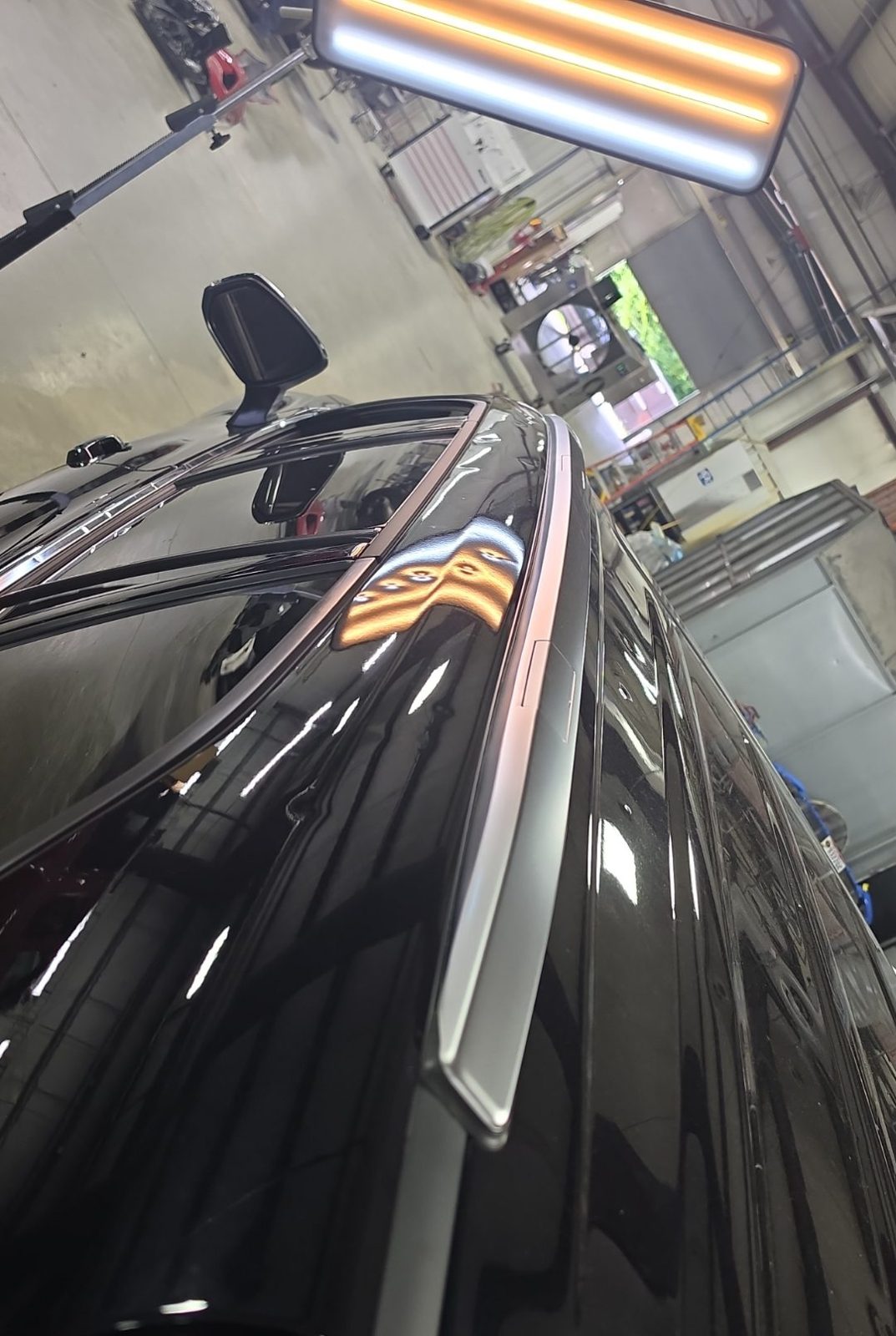 Driver roof rail of a black 2025 Toyota Highlander Hybrid with a PDR light board on a stand above it
